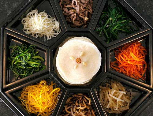 검은 구절판의 여러 칸에 흰색과 녹색, 주황색, 노란색 재료를 나누어 담은 모습